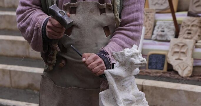 Artist carving small sculpture with hammer and chisel at medieval market Caravaca de la Cruz in Mercia, Spain in slow motion