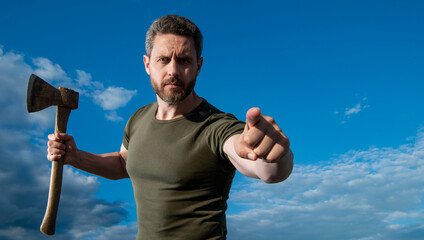man threaten with axe. caucasian man hold ax. brutal man on sky background. pointing finger
