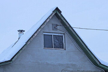 one gray concrete attic of an old private rural house with a small window with white snow on the roof against the sky on a winter street