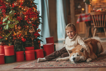 Candid authentic happy little boy in knitted beige sweater hugs dog with bow tie at home on Xmas