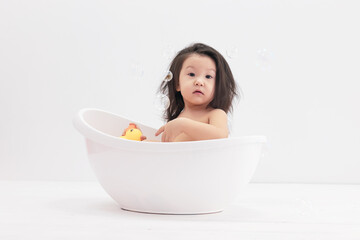 Little Asian girl takes a bath and plays duck toy. She is sitting in the bath.