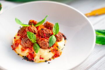 Beef meatballs in tomato sauce with mashed potatoes and basil in a white plate