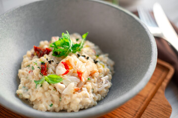 Risotto with crab meat and vegetables is served in a bowl. Dish with rice and seafood close up