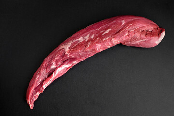 A whole piece of raw beef tenderloin on a dark table in the kitchen.