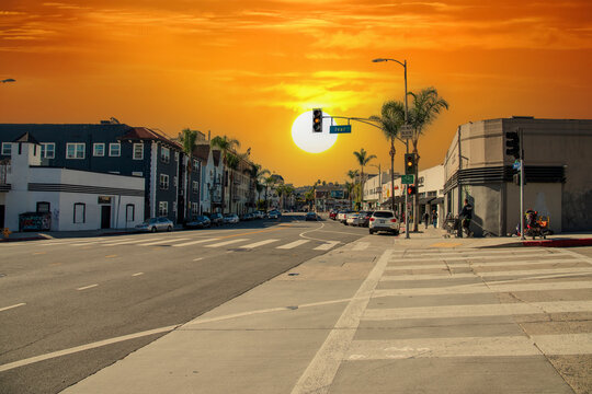 an intersection at Ivar Ave and Yucca street with apartments, shops, lush green palm trees, cars parked and driving, a homeless man with two shopping carts in Hollywood with powerful clouds at sunset