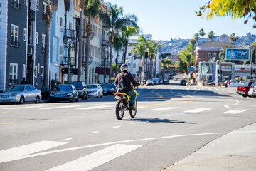 a man riding a yellow dirt bike on the street with parked cars, lush green palm trees, apartments and shops in Hollywood with a clear blue sky in Los Angeles California USA - obrazy, fototapety, plakaty