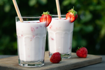Strawberry smoothie in two glass glasses and fresh strawberries on a wooden table in the yard