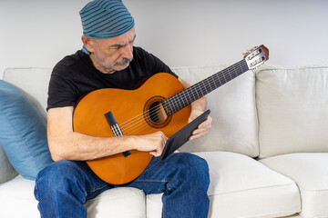 Old Man Practicing to Play Guitar Sitting on Sofa at Home
