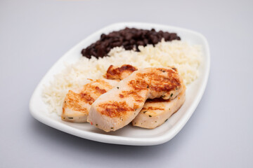 Healthy food with chicken breast, beans and rice on a white plate.