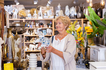 Portrait of senior woman choosing decorative statue for home at store of household goods