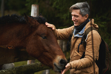 Adult man with happy emotions stroking horse head, brown horse licking his hand. Human and animal...