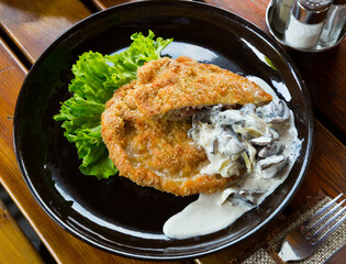 Delicious dinner pork schnitzel served with creamy mushroom sauce and greens