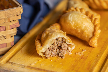 Close up of fried Argentine empanada cut in the middle on a wooden board.