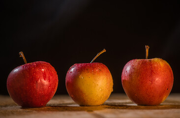 three apples on a wooden table with a dark background front view of apples
