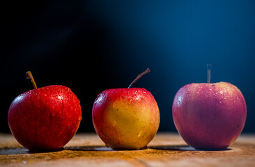 three apples on a wooden table with a dark background front view of apples