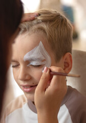 Master making aqua makeup on boys face. face painting kids. Child animator, artist's hand draw face...