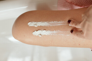 girl smears white cosmetic cream on her leg