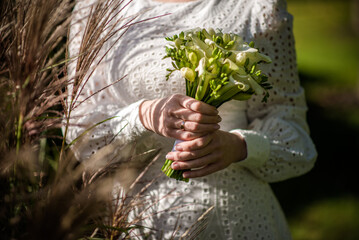 The bride in a white wedding dress is holding a bouquet of white flowers - peonies, roses. Wedding. Bride and groom. Delicate welcome bouquet. Beautiful decoration of weddings with leaves