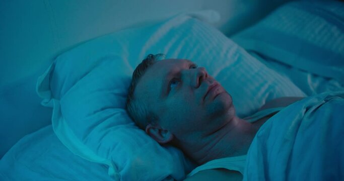 Depressed man suffering from insomnia lying in bed. Medium shot