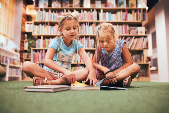Two schoolgirls reading books in school library. Primary school students learning from books. Pupils doing homework. Children having fun in school club. Back to school