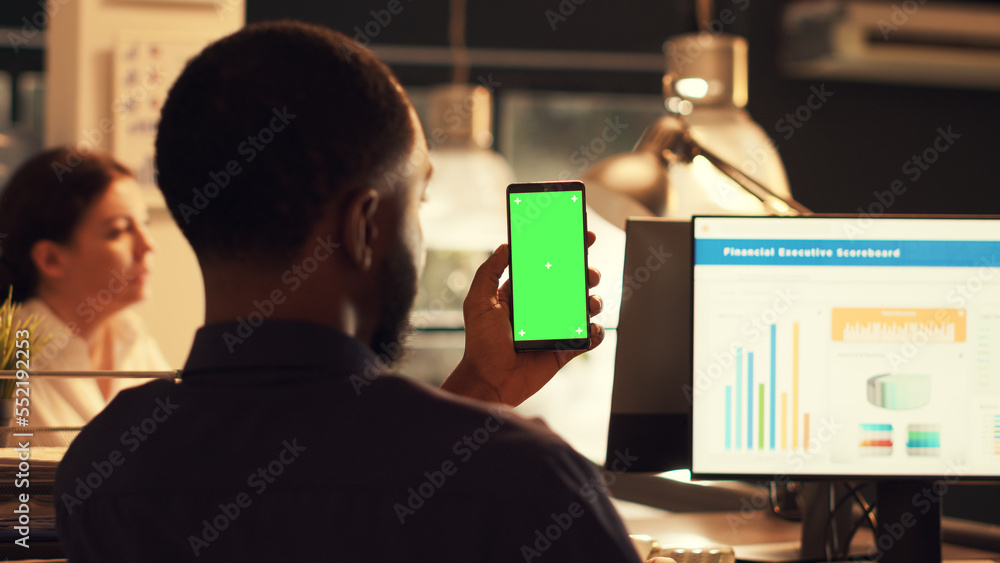 Poster startup employee holding smartphone with greenscreen and working on company data, looking at isolate