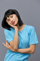 a peaceful woman stands against a dark background in a blue T-shirt and puts her head on the palm of her hand holding it with her other hand