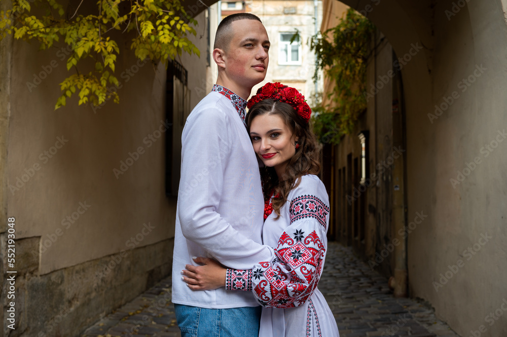 Wall mural A happy young couple in love, a family walking through the old city of Lviv in Ukrainian embroidered dresses, holding hands. Young people hug in the old town of Lviv
