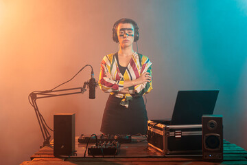 Female performer posing with arms crossed at turntables, using headphones and mixer to produce...