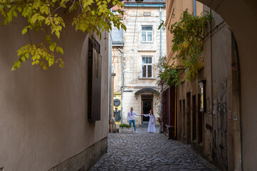 Fototapeta na wymiar A happy young couple in love, a family walking through the old city of Lviv in Ukrainian embroidered dresses, holding hands. Young people hug in the old town of Lviv 