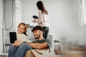 Obraz premium Father and daughter having fun in new apartment, while mother in the background unpacking stuff