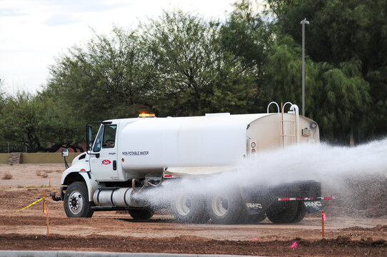 White water truck spraying water to suppress dust on a dirt road at construction site
