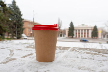 Winter. Cold weather. A cup of coffee stands on the ground against the backdrop of a city street