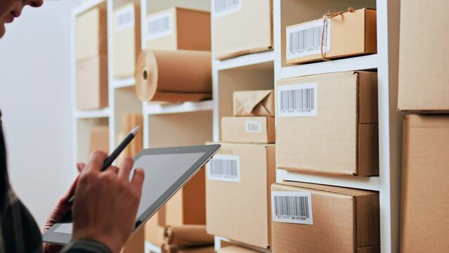 Girl warehouse worker of small medium-sized business in the process of accounting for goods in a warehouse, Hands hold an electronic tablet analysis of boxes with code placed on the shelves of rack
