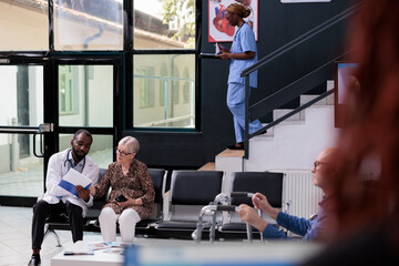 Elderly patient patient looking at papers with medical report while physician explaining medication...
