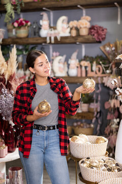 Positive young woman choosing christmas tree decorations in store.
