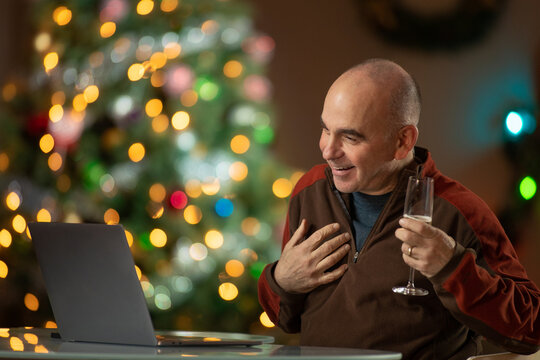Middle aged man with Champagne having fun on a zoom call in front of the Christmas Tree
