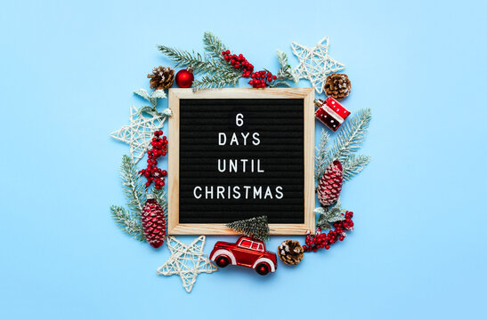Black board with letters with countdown surrounded by winter seasonal decoration on blue background. 6 days until Christmas. Twenty-four day series of postcards. Selective focus