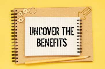 Uncover the Benefits - text written on notebook on wooden table with pen coffee and glasses.