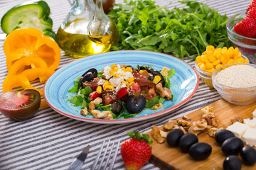Rocket salad with vegetables and soft cheese served in ceramic dish on striped textile on background with fresh ingredients