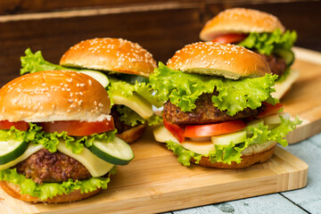 Delicious burgers with lettuce and cheese served on cutting board