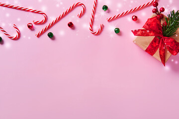 Christmas composition. Border made of candy canes and gift box, holiday decorations on a pink background.