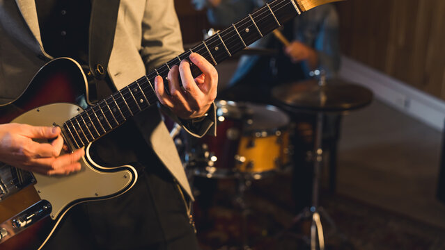 Close up of a man hands playing electric guitar inside a music band. High quality photo