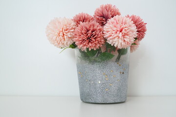 Bouquet of pink terry artificial flowers in a gray silver vase on a white background. Still life,...