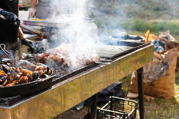 Defocus man cooking bbq meat at festival outdoor. Seafood paella. Chef grilling sausages in park outside. Concept of summer party with families and friends. Food festival. Out of focus