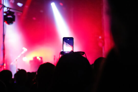 Defocus people holding their smart phones and photographing concert. Close up of photographing with smartphone during a red concert. Out of focus
