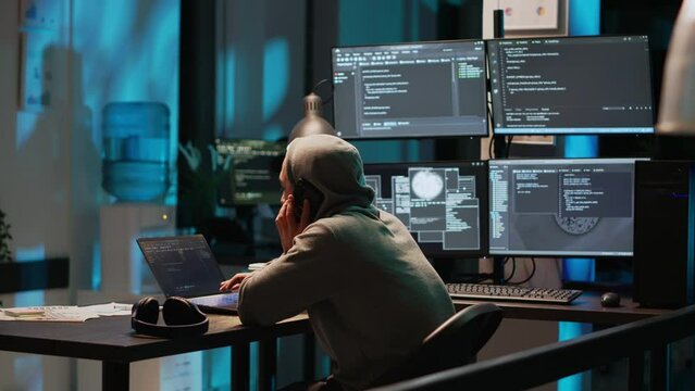 Young programmer answering phone call in office, talking on smartphone and coding user interface. Having remote conversation on mobile phone line, using html script on terminal window.