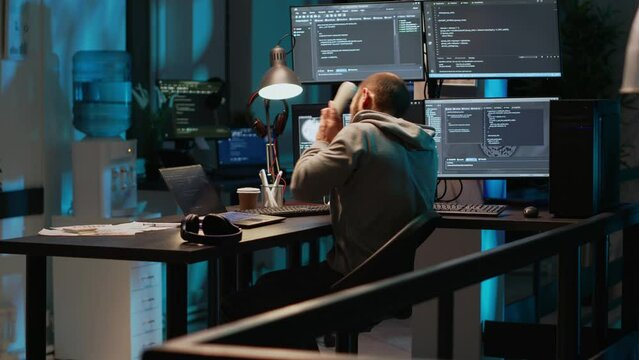 Young adult coder talking on landline phone at night, answering phone call in office. Male programmer using telephone with cord to chat and work on online cloud computing, artificial intelligence.