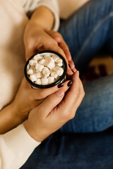 The hands of a man and a woman hold a mug with a hot drink and marshmallows
