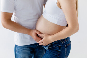 A pregnant woman and a loving husband hugs her stomach on a white background. The feeling of the baby's movement by a couple on the pregnant woman's stomach. Close-up.