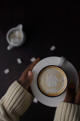 Female hands holding a cup of coffee with marshmallow in the cup